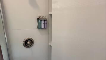 A bathroom with a shower, a toilet, and a shelf with toiletries.