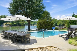 A poolside area with a table and chairs, umbrellas, and a view of a lake. - Completely Renovated - Ideal for up to 16 with private pool, hot tub, arcade and great amenities! (Denver)
