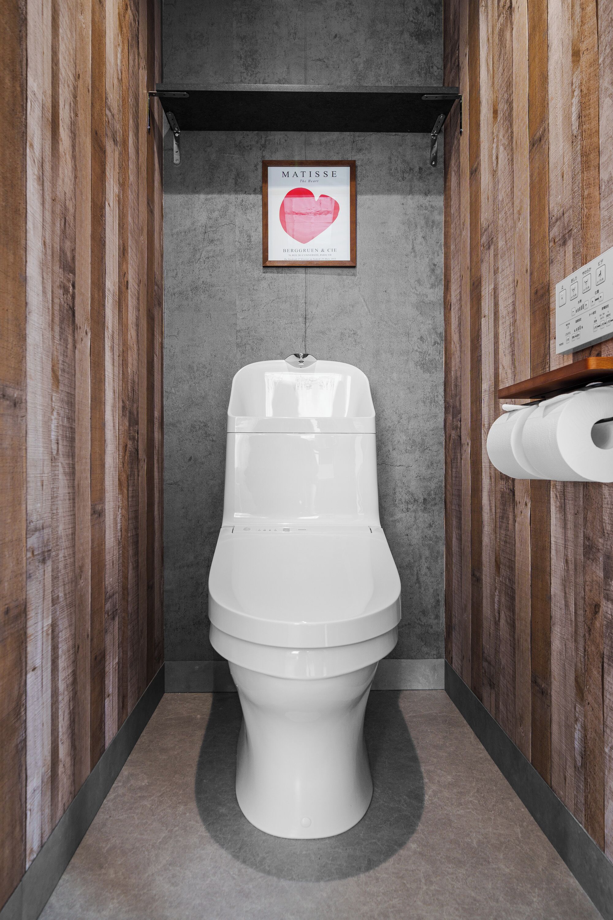 A modern bathroom with a white toilet, wooden panel walls, a concrete floor, and a framed picture on the wall.