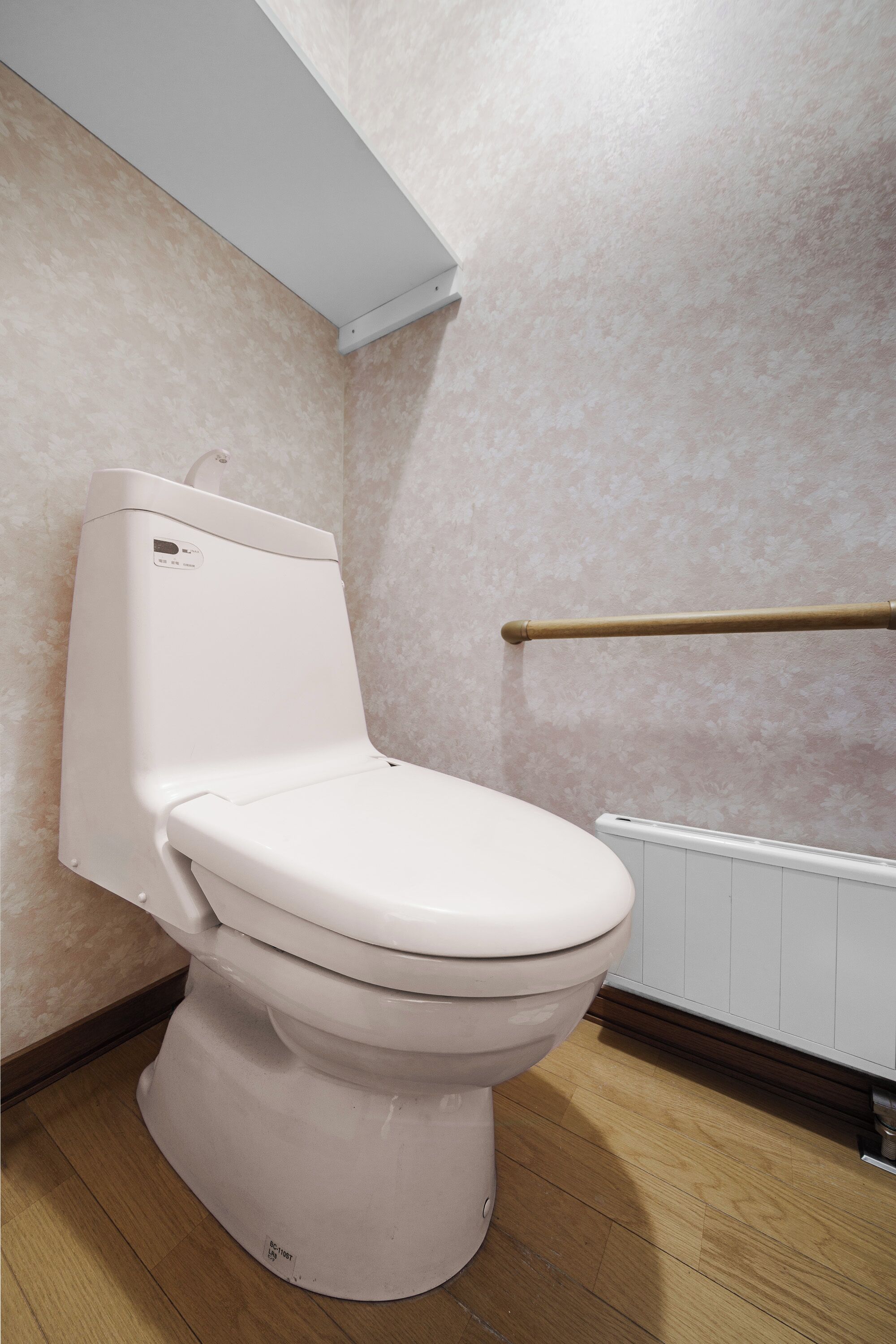 A white toilet in a bathroom with a wooden floor and a radiator.