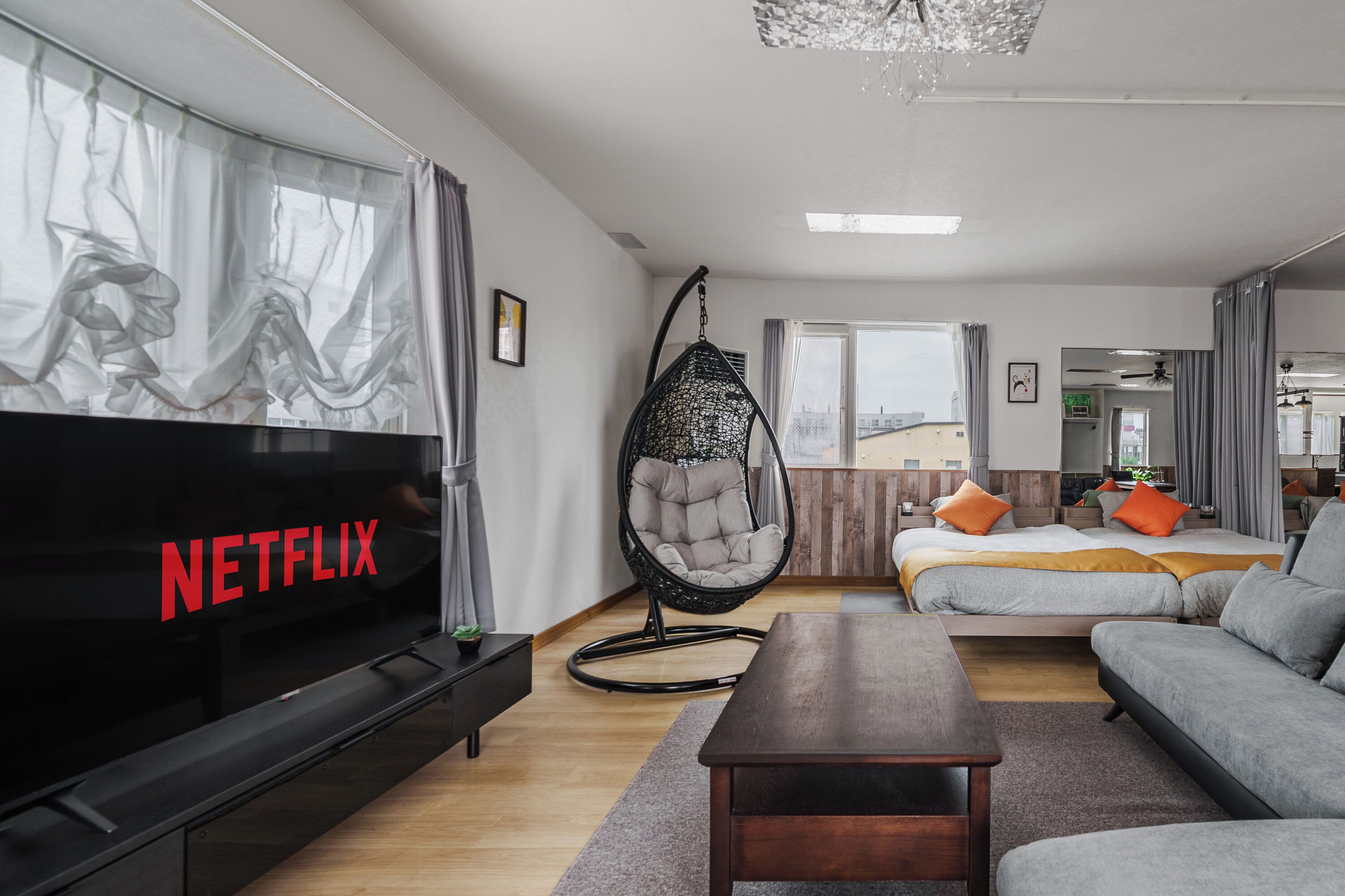A modern living room with a flat-screen TV, a hanging chair, a sofa, a bed, and a dining table.