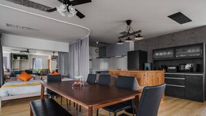 Un espacio de estar moderno con comedor, cocina y una cama grande con almohadones naranjas.