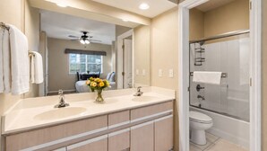 Une salle de bain avec un meuble-lavabo à deux vasques, un espace douche et un ventilateur de plafond.