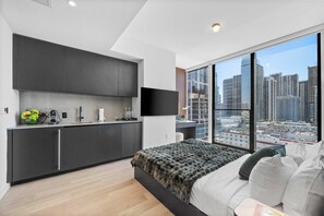 A modern bedroom with a large bed, a city view, a kitchenette, and a flat-screen TV. - Elite E11EVEN Grand Suite Rooftop Pool and City Views (Miami)