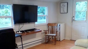 Una habitación con televisión, una silla, un sofá y un escritorio.