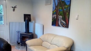 Una sala de estar con un sofá, una mesita, un radiador, una chimenea y un cuadro en la pared.
