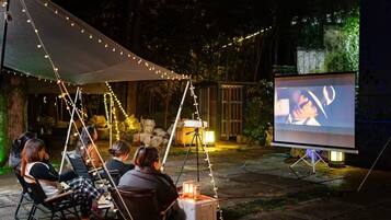 An outdoor movie screening setup with a projector and screen, surrounded by string lights and seating.