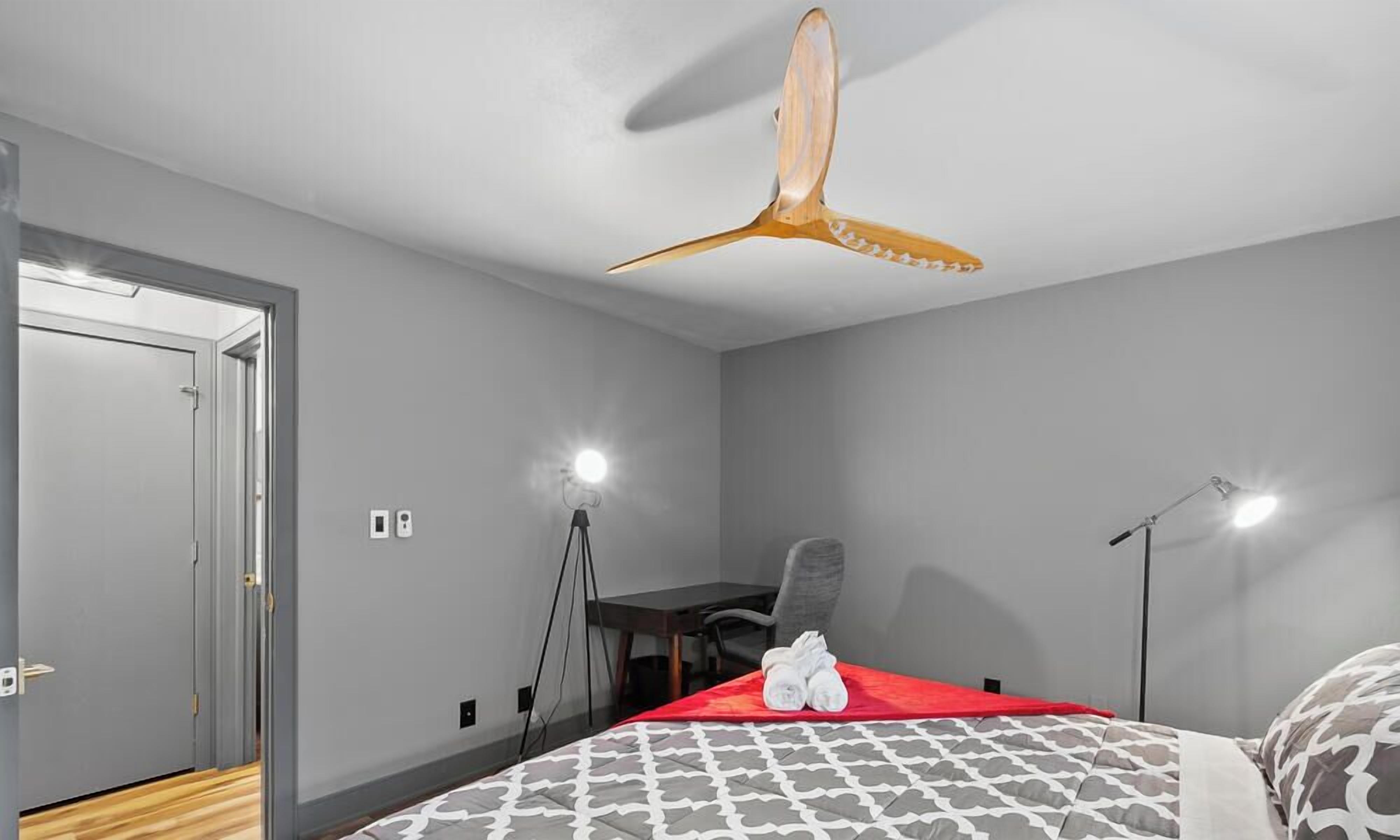 Ein Hotelzimmer mit einem Bett, einem Schreibtisch, einem Sessel, einem Deckenventilator und einer Tür.