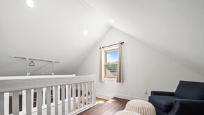 Una habitación con techo blanco, ventana con vistas, barandilla blanca y un sofá de color oscuro.