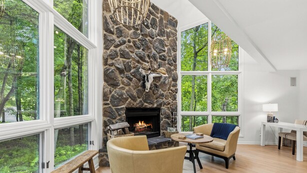 A room with a stone fireplace, large windows, a dining area, and a view of the outdoors. - Fontana Home With Pool and Hot Tub Minutes from the Lake (Fontana-on-Geneva Lake)