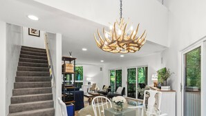 A spacious dining area with a glass table and white chairs, a staircase with a dark carpet, and a large chandelier. - Fontana Home With Pool and Hot Tub Minutes from the Lake (Fontana-on-Geneva Lake)