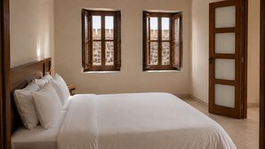 A bedroom with a bed, pillows, a nightstand, two windows with shutters, and a door with frosted glass panels. - Perfect 4-bedroom house with AC in enchanting Cartagena (Cartagena)