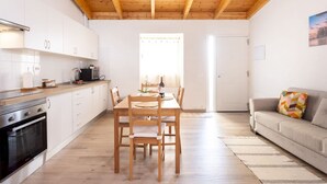 A modern kitchen with white cabinets, a wooden dining table, and a sofa with a colorful cushion. - Coqueta Casita de Mercedes (Tacoronte)