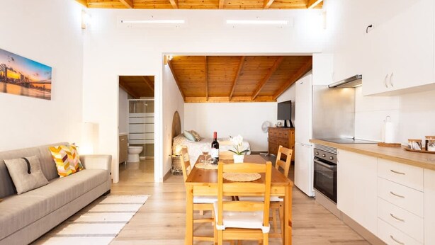 A modern kitchen with wooden cabinets, a dining area with a wooden table and chairs, and a sofa in the living room. - Coqueta Casita de Mercedes (Tacoronte)