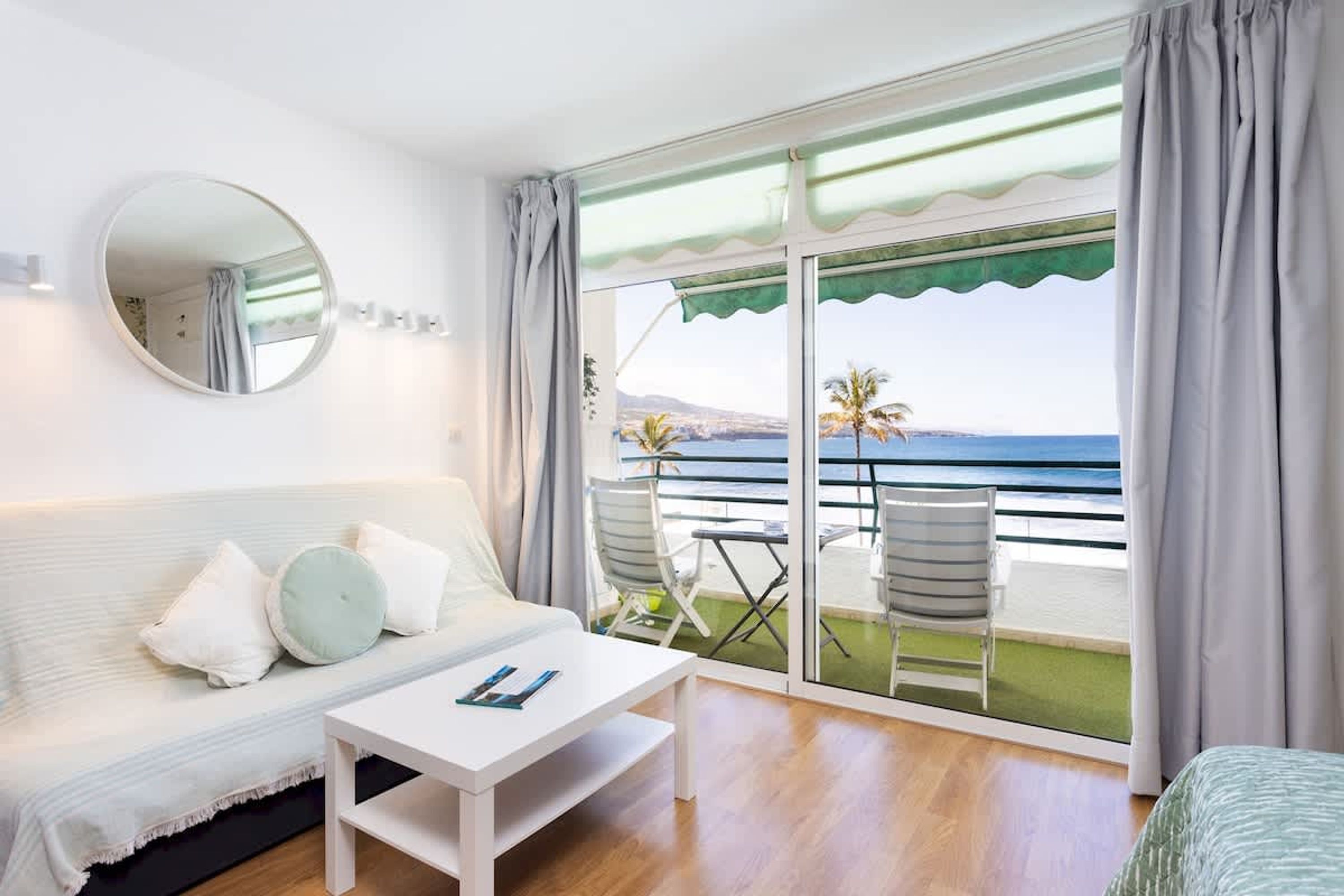 Habitación de hotel con balcón, un sofá, una mesa y vista al mar.