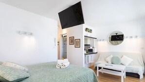 A bedroom with a bed, a white sofa, a TV, a kitchen area, and a bathroom. - Punta Para so in Punta del Hidalgo (San Cristóbal de La Laguna)