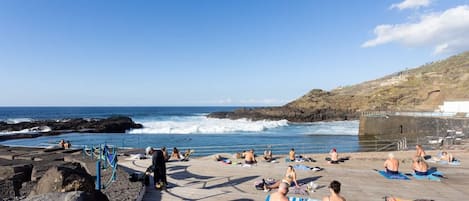 A beach with people sunbathing, a wooden boardwalk, and rocky terrain.