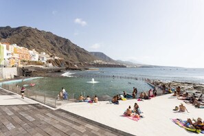 Eine Uferpromenade mit Schwimmbad, Strand und Gebäuden im Hintergrund.