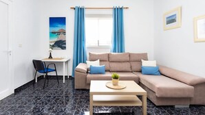 Ein Wohnzimmer mit einer Couch, einem kleinen Tisch, einem Stuhl, einem Schreibtisch und einem Fenster mit Vorhängen.