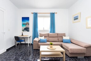 Ein Wohnzimmer mit einer Couch, einem kleinen Tisch, einem Stuhl, einem Schreibtisch und einem Fenster mit Vorhängen.