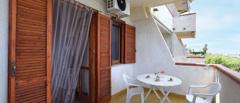 A balcony with wooden shutters, a table with chairs, and an air conditioning unit.