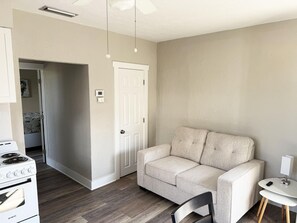 Eine moderne Küche mit einem Avanti-Herd, einer weißen Tür und einem beige gefärbten Sofa in einem neutralen Raum.