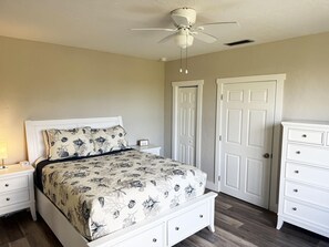Une chambre à coucher comprenant un lit, deux tables de chevet, une commode, un ventilateur de plafond et deux portes.