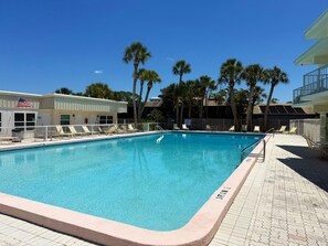 Ein Swimmingpool mit Liegestühlen, ein Gebäude mit einer amerikanischen Flagge und Palmen.