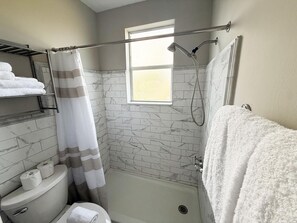 Une salle de bain avec une douche, des toilettes et une fenêtre.