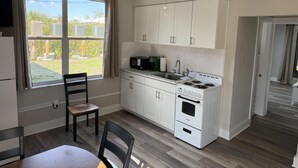 A compact kitchen with white cabinets, a stove, a microwave, and a window with curtains. - Venice Villas San Marco - Golden Beach (Venice)