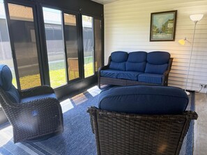 Ein Zimmer mit einem blauen Sofa, Korbstühlen und einem großen Fenster mit Jalousien.