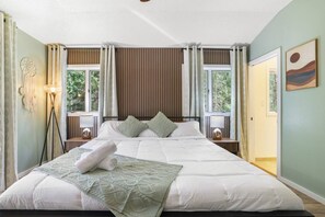 A bedroom with a large bed, two bedside tables with lamps, a floor lamp, and a window with curtains. - Contemporary Home in Pocono Farms Country Club Near Kalahari & Camelback (Tobyhanna)