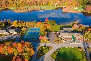 An aerial view of a golf course with a tennis court, a pond, and surrounding autumn foliage. - Contemporary Home in Pocono Farms Country Club Near Kalahari & Camelback (Tobyhanna)
