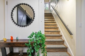 A staircase with wooden steps and a metal handrail, a wooden bench with decorative bird figurines, and a mirror with a black bead frame. - Contemporary Home in Pocono Farms Country Club Near Kalahari & Camelback (Tobyhanna)