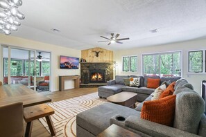 A spacious living room with a fireplace, a large sofa, a dining table, and a ceiling fan. - Contemporary Home in Pocono Farms Country Club Near Kalahari & Camelback (Tobyhanna)
