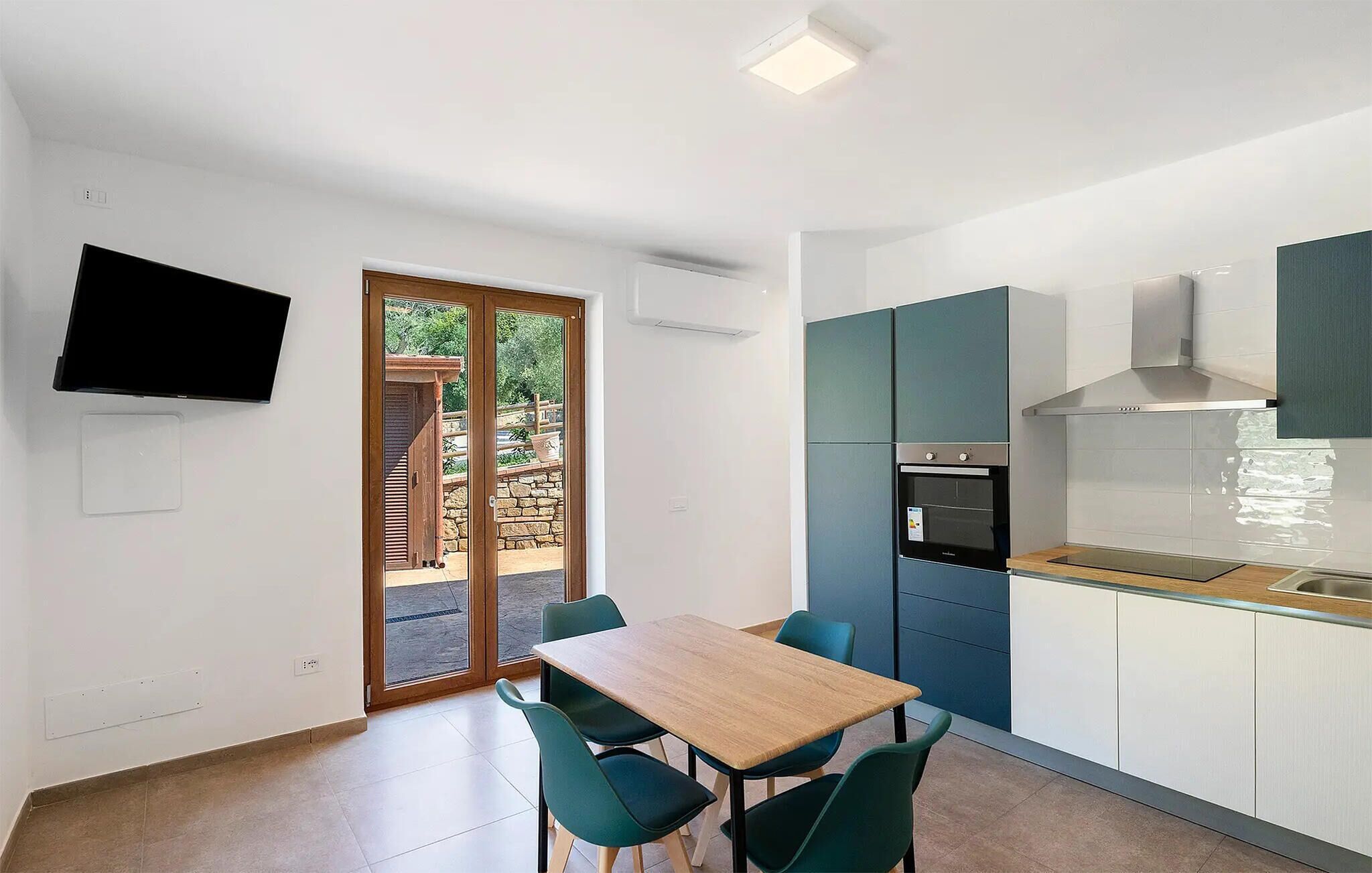 A compact kitchen with a built-in oven, a dining area with a table and chairs, and a TV mounted on the wall.