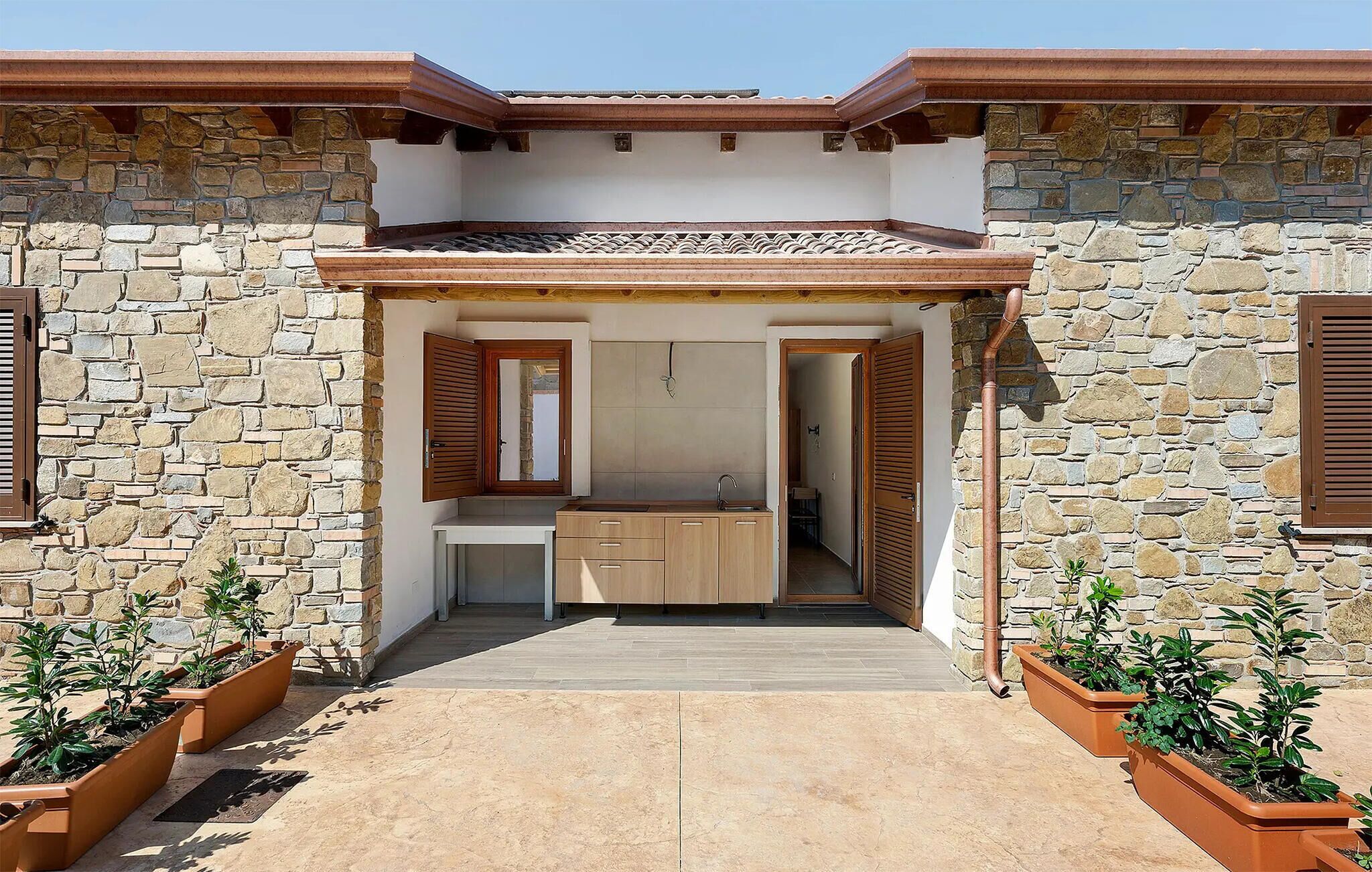 A stone building with a kitchen area, wooden shutters, and potted plants.