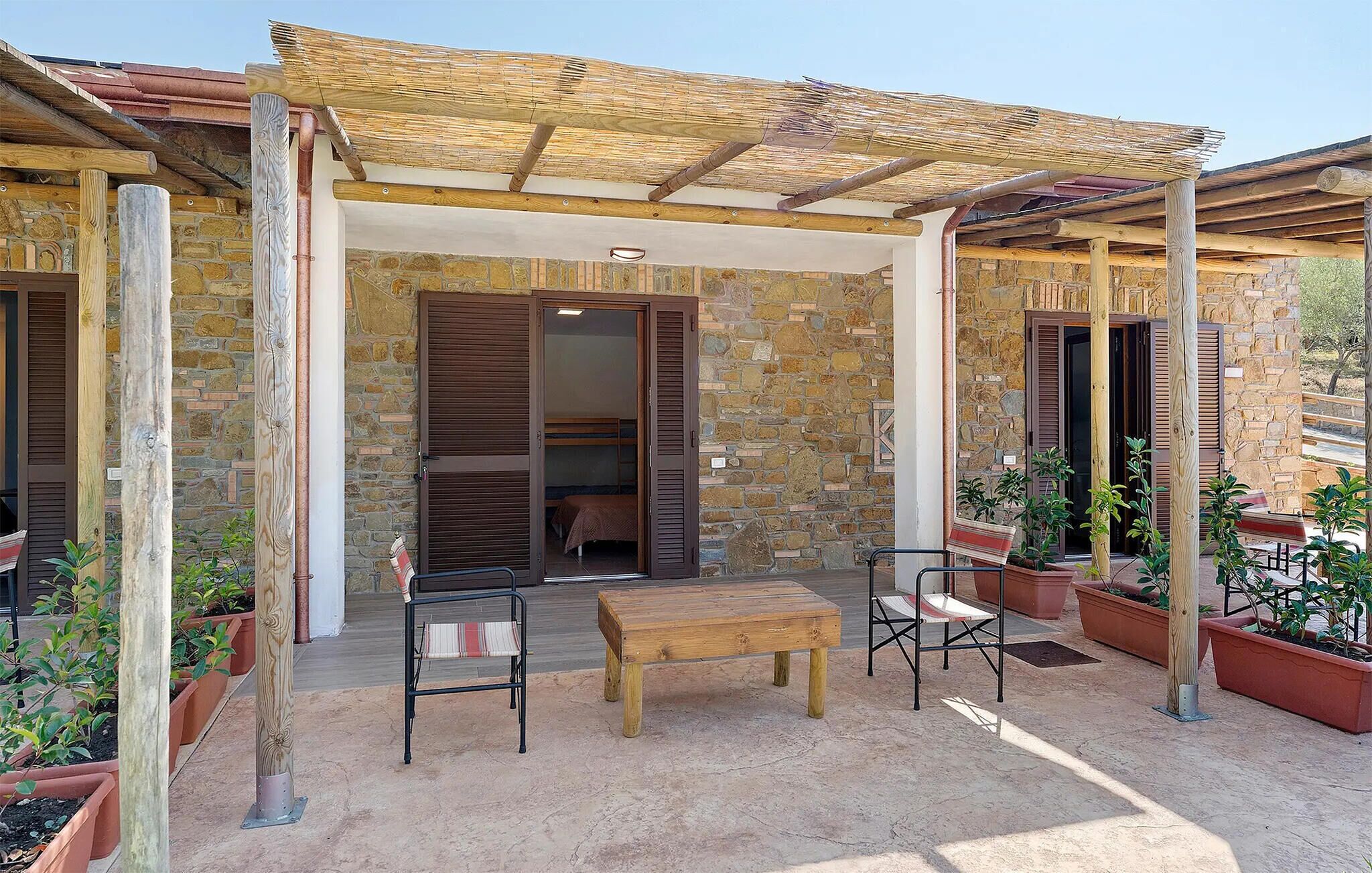 A covered outdoor seating area with a stone wall, wooden furniture, and potted plants.