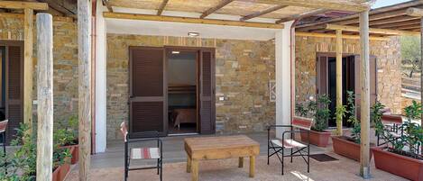 A covered outdoor seating area with a stone wall, wooden furniture, and potted plants.