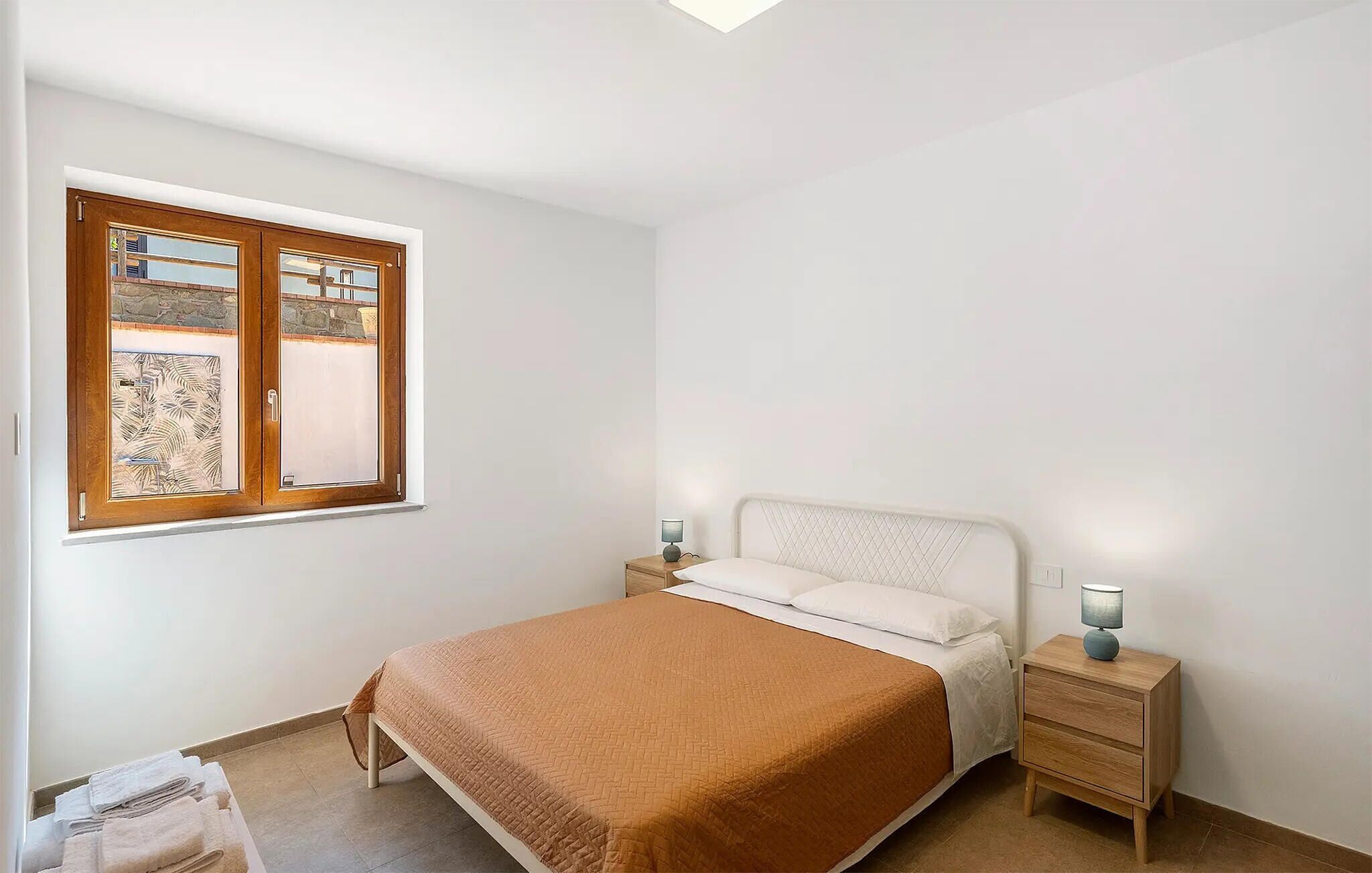 Une chambre à coucher avec un lit, deux tables de chevet, une fenêtre donnant sur un beau paysage et une petite table de chevet avec une lampe.
