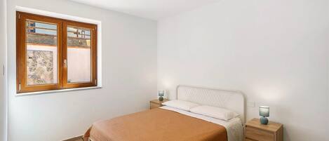 A bedroom with a bed, two bedside tables, a window with a view, and a nightstand with a lamp.