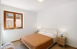 Ein Schlafzimmer mit einem Bett, zwei Nachttischen, einem Fenster mit Blick und einem Beistelltisch mit Lampe.