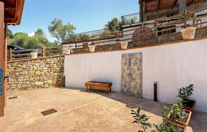 A stone wall, a bench, a patterned wall, and potted plants in a courtyard. - Nice home in Marina di Casal Velino with WiFi (Marina di Casal Velino)