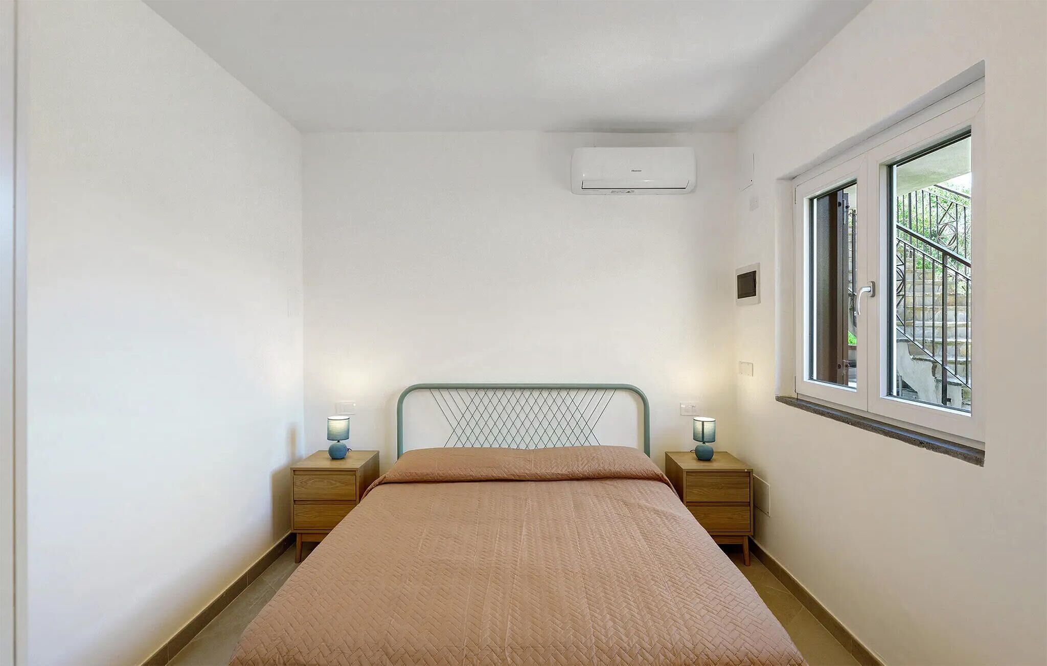 A bedroom with a bed, two bedside tables, a window, and an air conditioning unit.