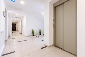 Un pasillo moderno de hotel con un ascensor cerrado, un camino despejado hacia una habitación y un pequeño arreglo de plantas.