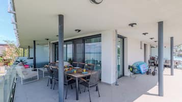 Un espacio de comedor al aire libre cubierto con mesa, sillas, un sofá y barandilla de vidrio.