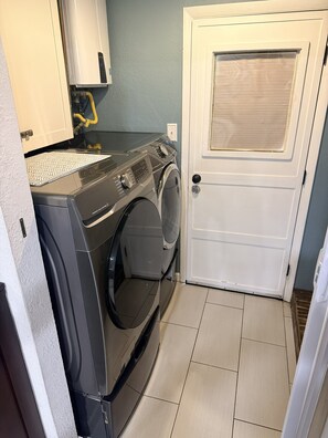 A laundry room with a front-loading washer and dryer, a white door, and a tiled floor.