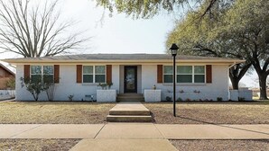 A single-story house with a front entrance, a small porch, and a front yard with a tree and shrubs.