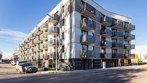 A modern multi-story building with balconies, a parking area, and a sign indicating a location. - Mostek Riverside Deluxe Studio (Gdańsk)