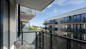 A balcony with a table and chairs, a view of a modern building, and a clear sky. - Mostek Riverside Deluxe Studio (Gdańsk)
